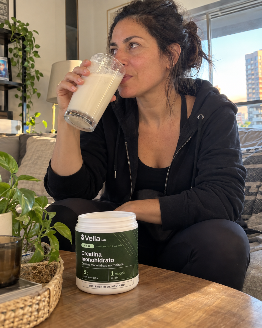 Mujer tomando un batido en el living, con el pote CR-02 en la mesa